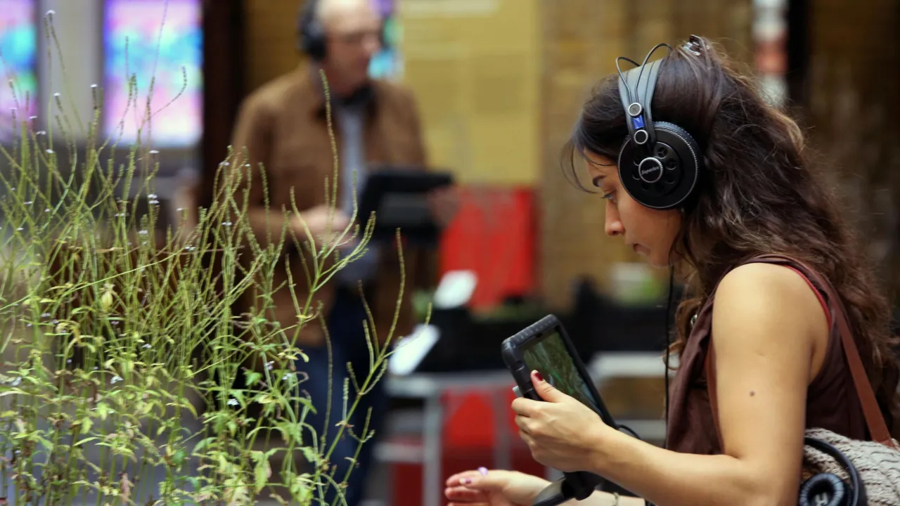 Vrouw met koptelefoon en tablet bij een plant, tijdens activiteit Praat eens met een plant van Chantalla Pleiter.