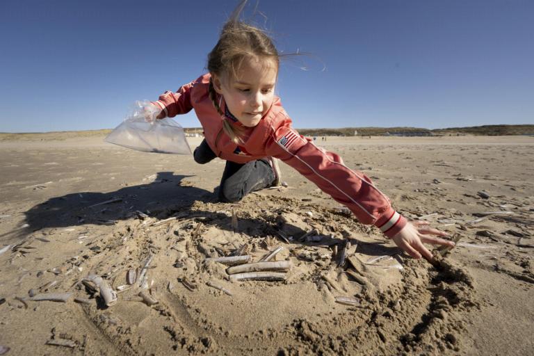 Een meisje tekent een spiraal in het zand om schelpen kunnen te tellen