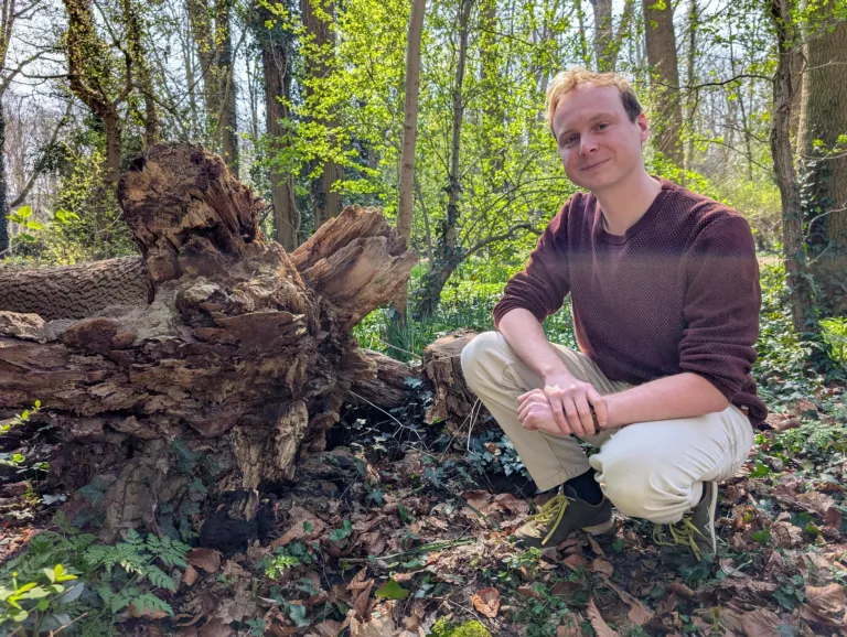 Portrain of Sjoerd next to a fallen tree with a mushroom growing between it's roots