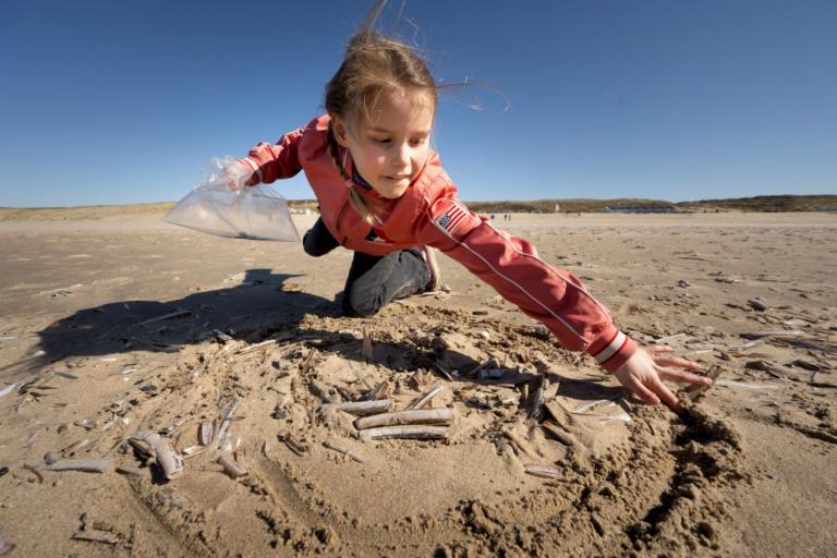 Meisje tekent spiraal in het zand om schelpen te verzamelen